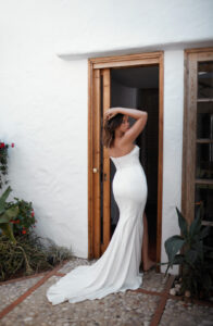 Dana Harel Danielle wedding dress from a bridal shop in Chicago. The model is showing the back of her dress and is standing barefoot in a wooden exterior door.