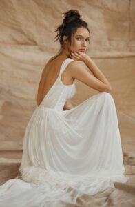 A model is crouched on the ground in front of drop cloths wearing a Nara by Dana Harel wedding dress from a bridal shop in Chicago, IL.