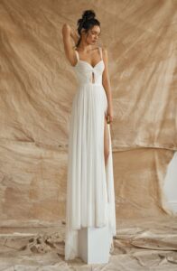 A model is standing on a ledge in front of drop cloths wearing a Nara by Dana Harel wedding dress from a bridal shop in Chicago, IL.