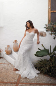 Dana Harel Venice Wedding Dress from a Bridal Shop in Chicago, IL. The model is leaning against a stucco staircase and is not looking at the camera.