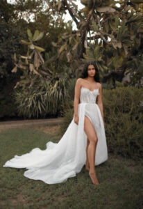 Dana Harel Kim wedding dress from a bridal shop in Chicago, IL. The model is standing barefoot in front of plants.