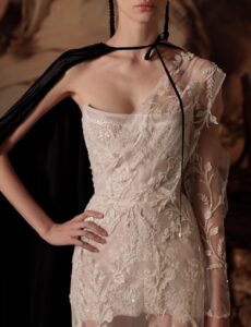 A close-up shot of the delicate mini wedding dress "Bonvolio" by designer Kim Kassas. This dress is has sheer embroidered fabric draped across one shoulder. It's available through Mira Couture in Chicago, IL