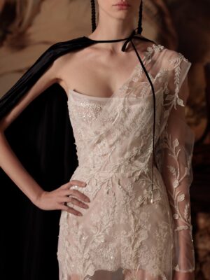 A close-up shot of the delicate mini wedding dress "Bonvolio" by designer Kim Kassas. This dress is has sheer embroidered fabric draped across one shoulder. It's available through Mira Couture in Chicago, IL