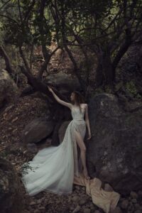 A model wearing a Kim Kassas Helice Wedding Dress with floral blush lace detailing, a high slit and dramatic overlay. Available at a bridal shop in Chicago, IL.