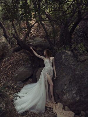 A model wearing a Kim Kassas Helice Wedding Dress with floral blush lace detailing, a high slit and dramatic overlay. Available at a bridal shop in Chicago, IL.