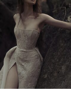 A closeup of a model wearing a Kim Kassas Helice Wedding Dress with floral blush lace detailing, a high slit and dramatic overlay. Available at a bridal shop in Chicago, IL.