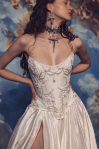 A model is wearing Kim Kassas's Isabelle strapless wedding dress with a high slit and detailed bodice with large religious jewelry