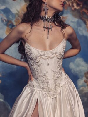 A model is wearing Kim Kassas's Isabelle strapless wedding dress with a high slit and detailed bodice with large religious jewelry