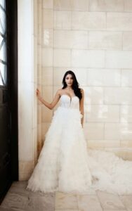 Martina Liana 1629 Wedding Dress is a tulle bridal gown featuring tiers of soft ruffles and a train at a bridal shop in Chicago, IL