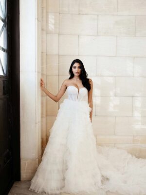 Martina Liana 1629 Wedding Dress is a tulle bridal gown featuring tiers of soft ruffles and a train at a bridal shop in Chicago, IL