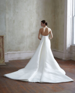 Back view of a model wearing a clean fit and flare gown featuring a classy crescent neckline and a detachable train from a bridal shop in Chicago, IL.