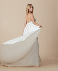 Side view of a model wearing Bobbi by Ti Adora Allison Webb, a fit and flare gown that features unique geometric embossed sateen fabric, crescent neckline, and a detachable train in Chicago, IL.