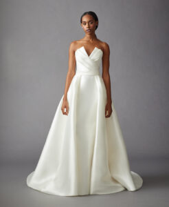 Full front view of a model wearing an A-line gown that features a pleated bodice, and detachable open overskirt from a bridal shop in Chicago, IL.