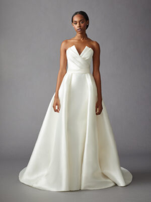 Full front view of a model wearing an A-line gown that features a pleated bodice, and detachable open overskirt from a bridal shop in Chicago, IL.