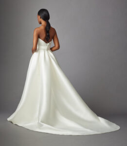 Back view of a model wearing a trumpet style gown that features a pleated bodice, and detachable open overskirt from a bridal shop in Chicago, IL.