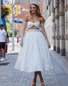 A model in Chicago, IL faces the camera in the Araceli by Calla Blanche wedding dress. It is a modern and flirty two-piece set that features a strapless sweetheart bodice and a vintage tea-length skirt.