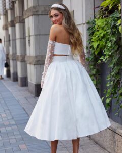 A model in Chicago, IL peaks over her shoulder in the Araceli by Calla Blanche wedding dress. It is a modern and flirty two-piece set that features a strapless sweetheart bodice and a vintage tea-length skirt.