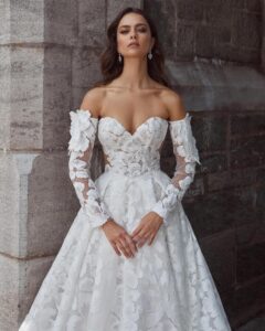 MMid-ground view of a model wearing a romantic sweetheart ballgown wedding dress with off-the-shoulder sleeves, delicate floral lace and a soft train from bridal shop Mira Couture in Chicago, IL.