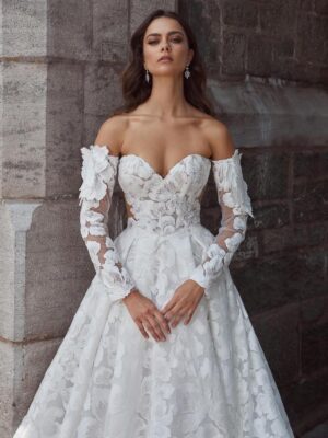 MMid-ground view of a model wearing a romantic sweetheart ballgown wedding dress with off-the-shoulder sleeves, delicate floral lace and a soft train from bridal shop Mira Couture in Chicago, IL.