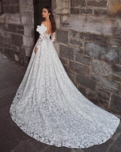 Full view of a model's back wearing a romantic sweetheart ballgown wedding dress with off-the-shoulder sleeves, delicate floral lace and a soft train from bridal shop Mira Couture in Chicago, IL.