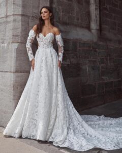 Full view of a model wearing a romantic sweetheart ballgown wedding dress with sleeves, delicate floral lace and a soft train from bridal shop Mira Couture in Chicago, IL.