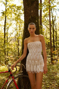 A bride standing next to a bike in the Daisy by Dana Harel wedding dress in Chicago, IL. The strapless mini dress that features glamorous pearl chains draped over the body.