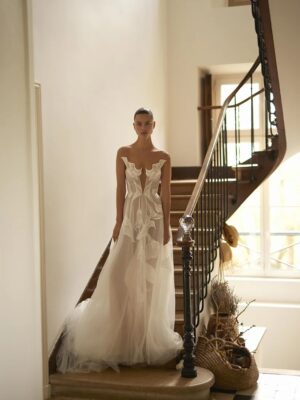 A bride wearing the Lily by Dana Harel wedding dress. It is a feminine soft A-line made out of a beautiful tulle skirt. It features delicate Calla Lily flowers cascading from the bodice down the train, creating an illusion-like painting on the body.