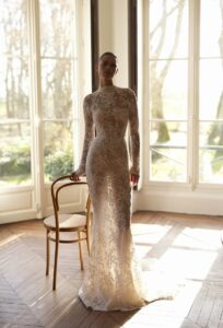 A bride shows the front of her Moe by Dana Harel wedding gown. It is an elegant fitted lace wedding dress made of sautage lace. Featuring a high collar neck and a classy open back.