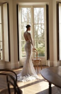 A bride shows the back of her Moe by Dana Harel wedding dress. It is an elegant fitted lace gown made of sautage lace. Featuring a high collar neck and a classy open back.