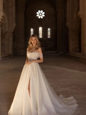 A model shows off Pelagia by Eva Lendel, a glamorous A-line gown with a dramatic glitter skirt featuring a leg slit and soft pearl embellished tulle cascading over the bodice and shoulders.