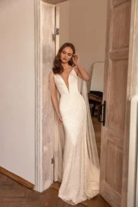 A model faces the camera and looks down while wearing the bold and glamorous beaded fitted gown Perla by Eva Lendel that features a plunge neckline and an elegant open back.