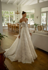 A bride shows the Pier by Neta Dover wedding dress. It's a romantic Chantilly lace ballgown featuring a sweetheart neckline and charming lace long sleeves. It's available at a bridal shop in Chicago, IL.