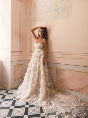 A bride leans against a wall wearing the Scarlet by Neta Dover wedding dress. This whimsical A-line bridal gown with delicate 3d floral embellishments features hand-sewn beading and a romantic sweetheart neckline. It is available at a bridal shop in Chicago, IL.