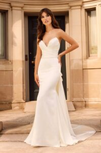 A bride rests a hand on her hip while showing her 5030 by Paloma Blanca wedding dress, an elegant and timeless satin fitted bridal gown with a romantic sweetheart neckline and a detachable satin train. It's available at a bridal shop in Chicago, IL.