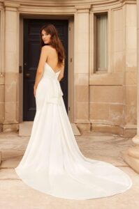 A bride peeks over her shoulder while showing her 5030 by Paloma Blanca wedding dress, an elegant and timeless satin fitted bridal gown with a romantic sweetheart neckline and a detachable satin train. It's available at a bridal shop in Chicago, IL.