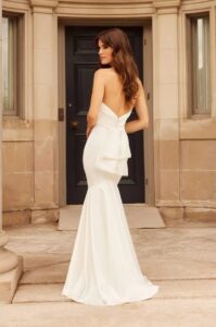 A bride shows her backless 5030 by Paloma Blanca wedding dress, an elegant and timeless satin fitted bridal gown with a romantic sweetheart neckline and a detachable satin train. It's available at a bridal shop in Chicago, IL.