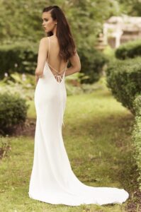 A model shows the back of the 5080 by Paloma Blanca wedding dress, a charmeuse satin bias cut gown featuring a V-neckline with a low back and delicate strap ties. It is available at a bridal shop in Chicago, IL.