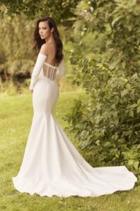 A model showcases the back of the 5083 by Paloma Blanca wedding dress. It is a sleek strapless princess cut bridal gown featuring a soft scoop neckline, corset back lined with Italian tulle, and detachable sleeves. This dress is available at a bridal shop in Chicago, IL.