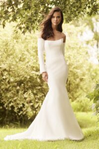 A bride wears 5083 by Paloma Blanca, a sleek strapless princess cut bridal gown featuring a soft scoop neckline, corset back lined with Italian tulle, and detachable sleeves. It is available at a bridal shop in Chicago, IL.