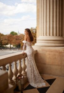 A model looks off of a balcony while wearing the Ellie by Eisen Stein wedding dress, a strapless fitted sequin dress with an elegant fold-over that is available at a bridal shop in Chicago, IL.