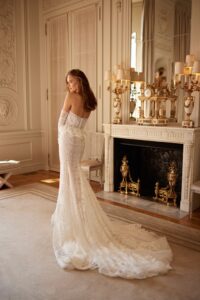 A model shows the train of her lace, fitted wedding dress with long sleeves, a sweetheart neckline, and a ruffle peplum belt available at a bridal shop in Chicago, IL.