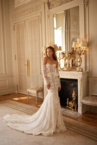 A model wears a lace, fitted wedding dress with long sleeves, a sweetheart neckline, and a ruffle peplum belt available at a bridal shop in Chicago, IL.