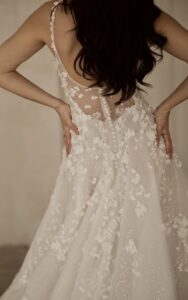 A bride shows the back of the 1718 by Martina Liana wedding dress with 3D floral details and a low back with buttons. This bridal gown is available at a bridal shop in Chicago, IL.