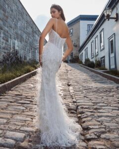 A bride shows the back of her fitted, sparkly wedding dress, 124125 Bryony by Calla Blanche. The bridal gown features feathers and spaghetti straps and is available at a bridal shop in Chicago, IL.