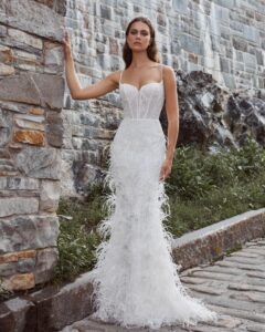 A bride stands outside showing her fitted, sparkly wedding dress, 124125 Bryony by Calla Blanche. The bridal gown features feathers and spaghetti straps and is available at a bridal shop in Chicago, IL.