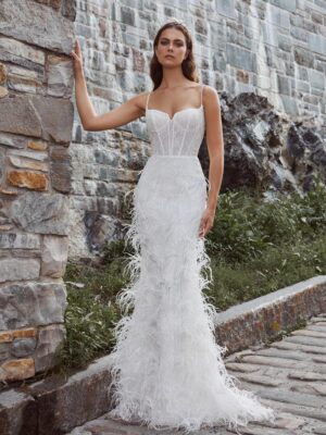 A bride stands outside showing her fitted, sparkly wedding dress, 124125 Bryony by Calla Blanche. The bridal gown features feathers and spaghetti straps and is available at a bridal shop in Chicago, IL.