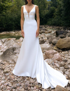 A bride shows the plunging neckline and train on her wedding dress, BRT 023 by Daalarna. This sleek A-line bridal gown features a low back and is available at a bridal shop in Chicago, IL.