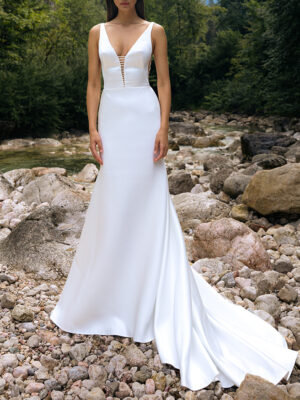 A bride shows the plunging neckline and train on her wedding dress, BRT 023 by Daalarna. This sleek A-line bridal gown features a low back and is available at a bridal shop in Chicago, IL.