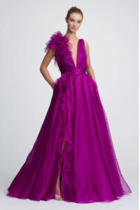 A bridesmaid shows the front of her bridesmaid's dress, 32821 by Marchesa. The stunning purple evening gown has a plunging neckline, a cascading ruffle, and a banded waist. See it at a boutique in Chicago, IL.