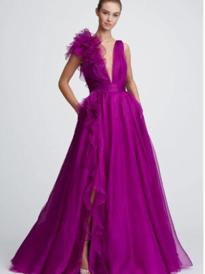 A bridesmaid shows the front of her bridesmaid's dress, 32821 by Marchesa. The stunning purple evening gown has a plunging neckline, a cascading ruffle, and a banded waist. See it at a boutique in Chicago, IL.